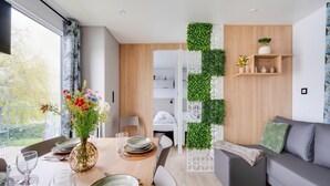 A modern dining area with a table set for four, a sofa, and a decorative wall with greenery. - Cozy Caravan in Berlare for 6 People (Berlare)