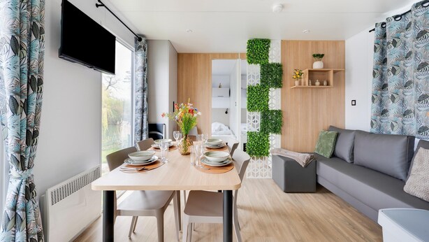 A modern living space with a dining area, a grey sofa, a wall-mounted green plant, and a flat-screen TV. - Cozy Caravan in Berlare for 6 People (Berlare)