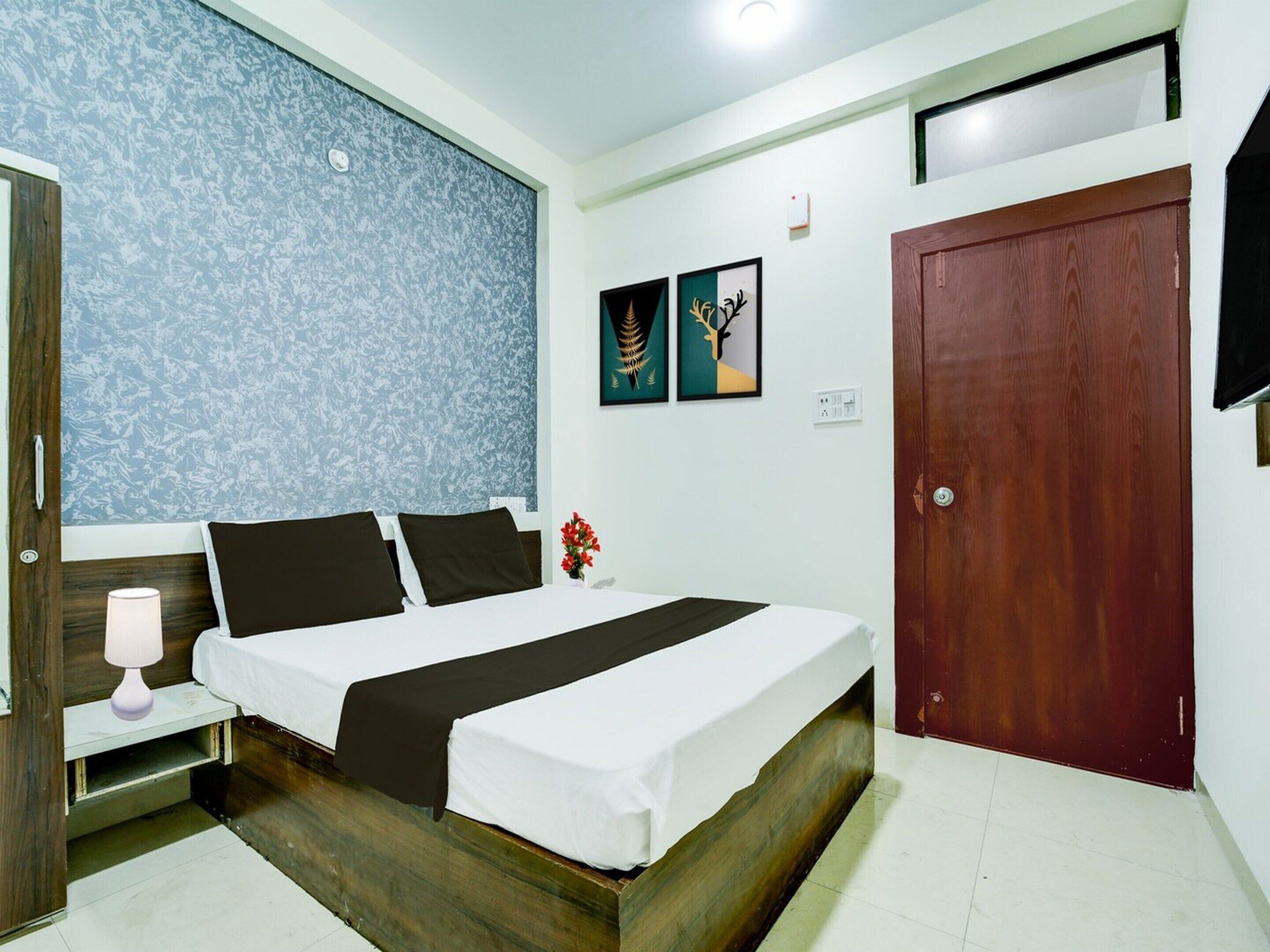 A bedroom with a bed, bedside table, lamp, wall art, and a door.