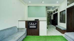 A reception area with a sign that reads 'Collection Company-Serviced,' a ceiling fan, a green carpet, and a hallway leading to a dark room. - Deluxe Hotel Sp14 (Indore)