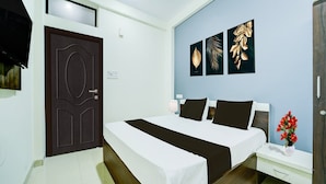 A hotel room with a double bed, a nightstand, a TV, and wall art. - Deluxe Hotel Sp14 (Indore)