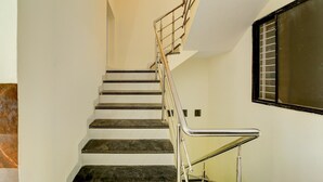 A staircase with a metal railing, white walls, and a window with blinds. - Deluxe Hotel Sp14 (Indore)