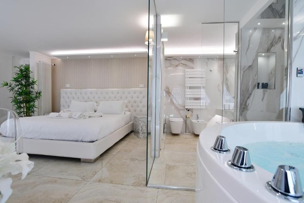 A modern bedroom with a large bed, a glass shower enclosure, and a separate bathroom with a bathtub.