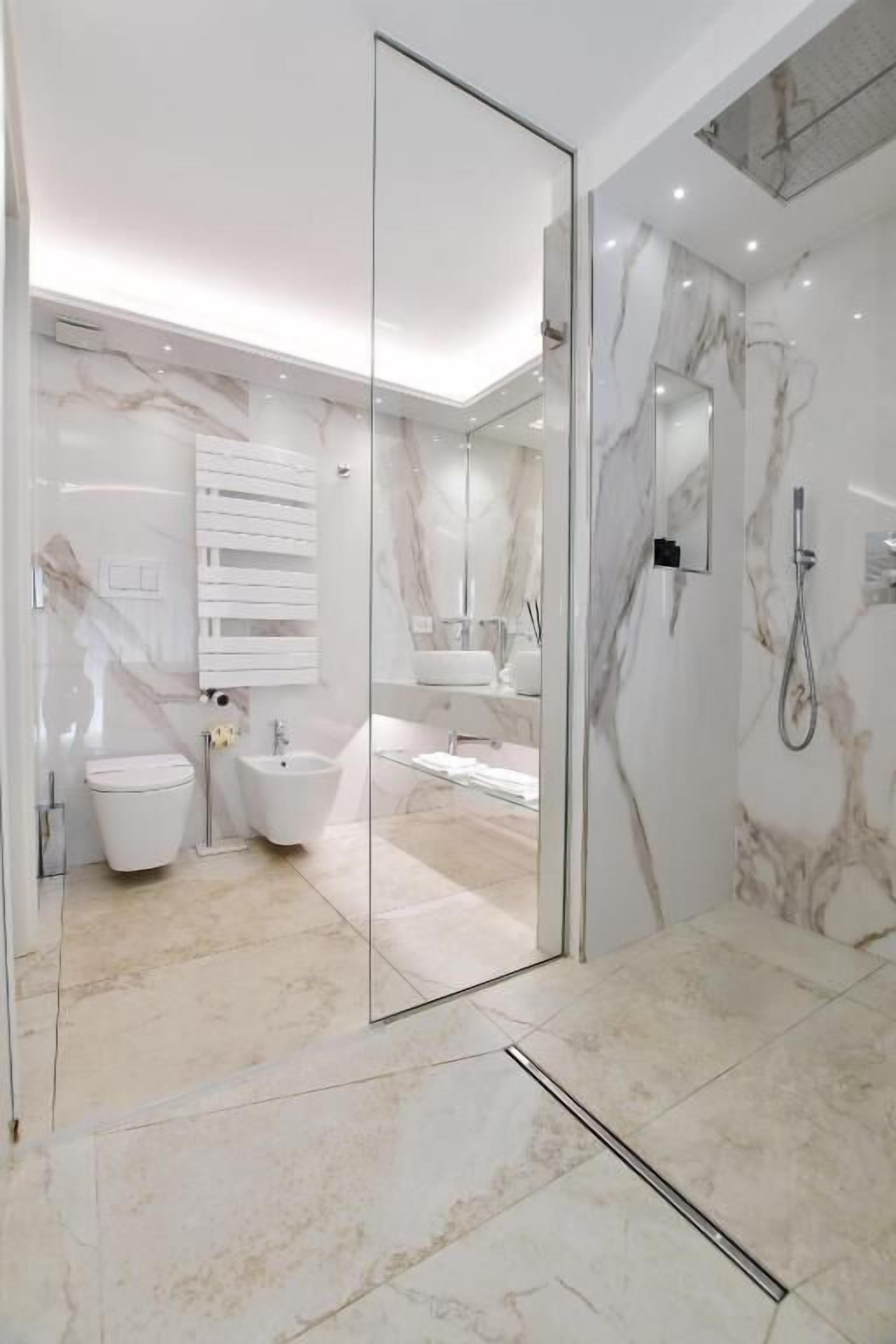 Un baño moderno con cabina de ducha de vidrio, un lavamanos blanco y piso de baldosas de mármol.