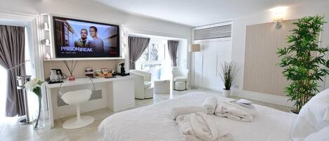 A hotel room with a bed, a desk, a TV, a chair, a plant, and a window.