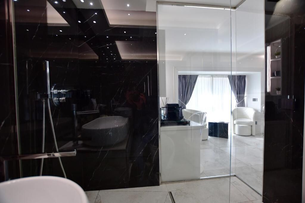 Un baño moderno con separador de vidrio, suelo de mármol y bañera blanca.