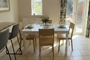 Un comedor con una mesa preparada para cuatro personas, sillas, un florero con una planta y una ventana con cortinas.