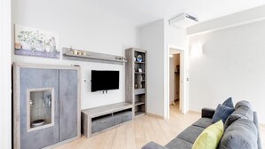 Een moderne woonkamer met een grijze bank, een flatscreen televisie, een houten kast en een boekenkast.
