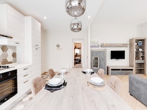Eine moderne Küche mit Einbauofen, ein Essbereich mit Holztisch für vier Personen und ein an der Wand montierter Fernseher.