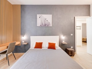 Ein modernes Schlafzimmer mit einem großen Bett, zwei Nachttischen, einem Schreibtisch und einem Sessel.