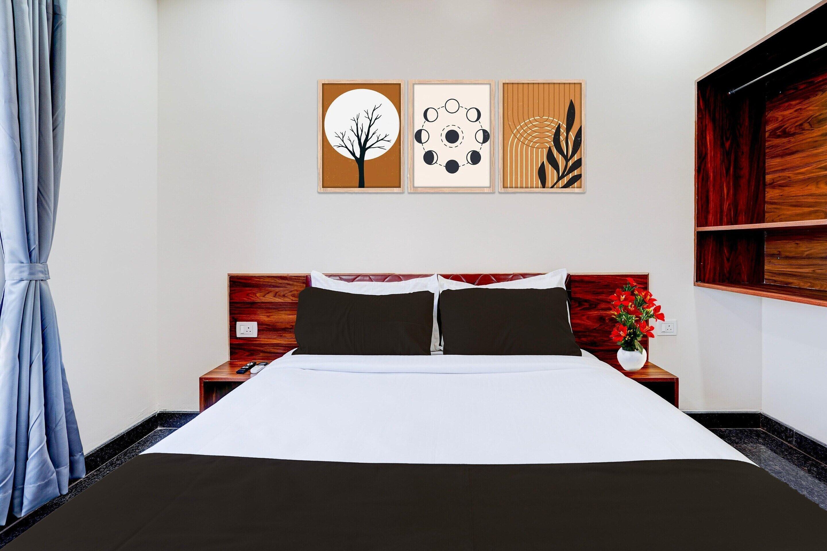 Una habitación de hotel con una cama, una mesita de noche, un televisor montado en la pared y una obra de arte sobre la cama.