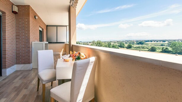 Varanda com uma mesa posta para dois, parede de tijolos e vista para o verde.