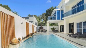 Un área de piscina moderna con una piscina cristalina, detalles de madera y una zona de estar con sillones reclinables.