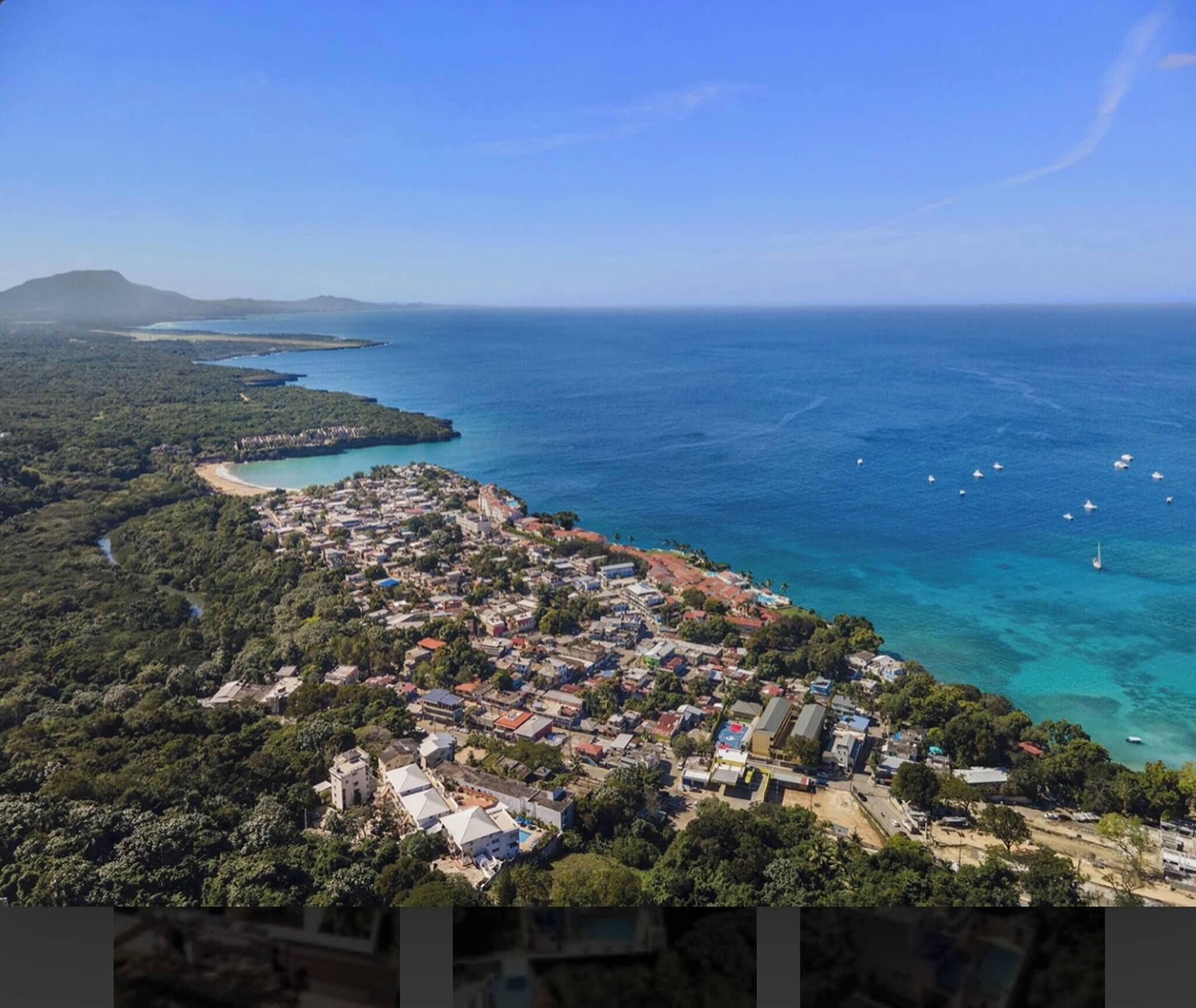 An aerial view of a coastal town with dense housing, a beach, and clear blue waters.