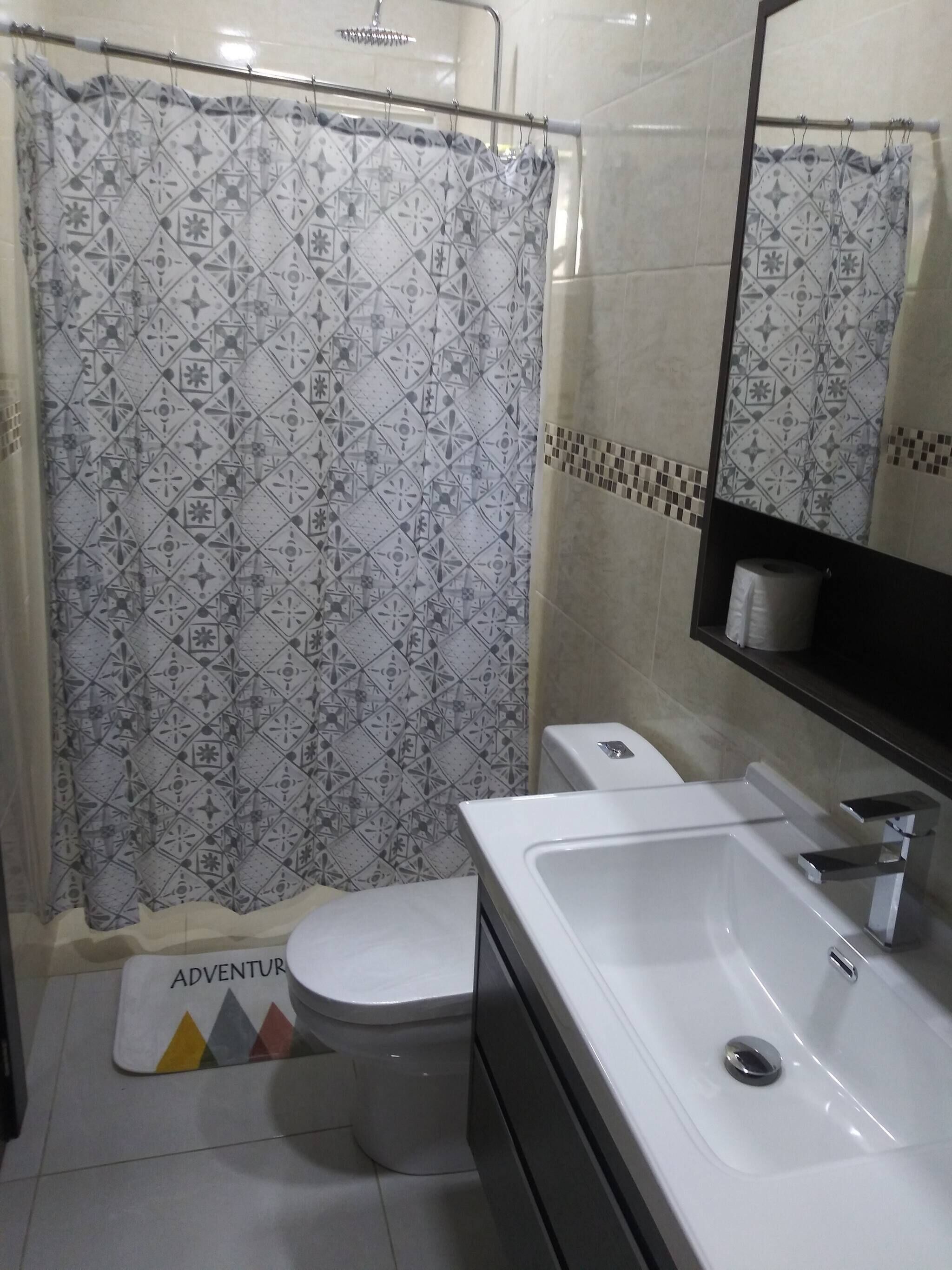 A bathroom with a shower curtain, toilet, sink, and a mirror.