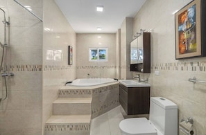 Un bagno moderno con una vasca da bagno ampia, uno spazio doccia separato, un mobile toilette con specchio e un water.