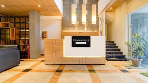 A reception desk with a sign reading 'TOWNHOUSE Company Serviced,' a staircase, and a reception area with a modern design. - Deluxe Ramora Grand (Thindukkal)