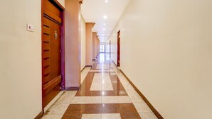 A hotel hallway with a checkered floor, wooden doors, and a light fixture on the ceiling. - Deluxe Ramora Grand (Thindukkal)