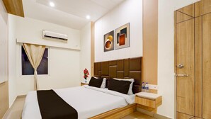 A modern hotel room with a large bed, a wooden headboard, a bedside table with a vase of flowers, and a wardrobe. - Deluxe Ramora Grand (Thindukkal)