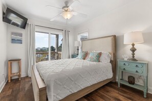A bedroom with a bed, a nightstand, a ceiling fan, and a view of the outdoors. - Waves on Willis | Hot Tub · Sound Views · 4BR AB (Atlantic Beach)