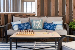 A sofa with a chessboard, pillows, and a small table with books and a plant.