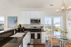 A modern kitchen with white cabinets, stainless steel appliances, a glass dining table, and a view of the outdoors.