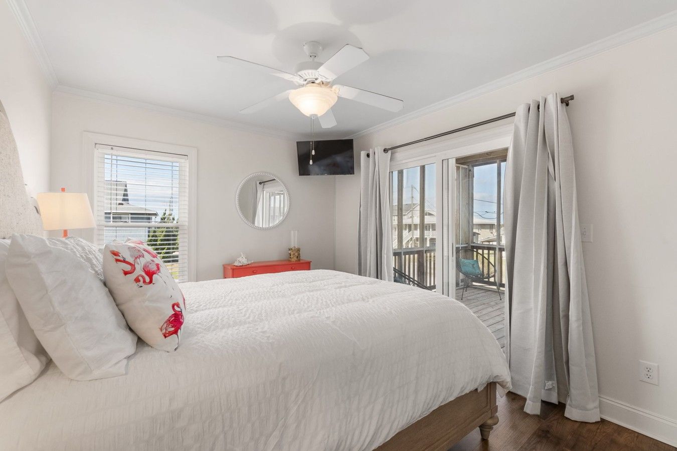Quarto com cama, ventilador de teto, televisão, janela com cortinas e varanda com cadeira.