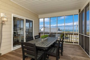 Un patio techado con mesa y sillas, ventanas amplias y vista al mar.