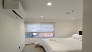 A bedroom with a bed, a window with blinds, an air conditioning unit, and a ceiling light.