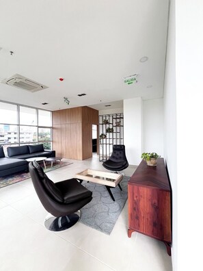 Un salon moderne avec un canapé, deux fauteuils noirs, une table basse en bois et une table d’appoint en bois agrémentée d’une plante.