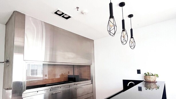 A modern kitchen with a stainless steel range hood, a black countertop, and hanging pendant lights.