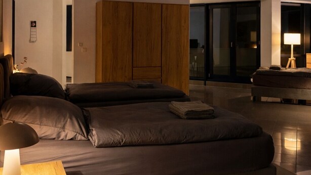 Un dormitorio moderno con una cama grande, cabecera de madera y vistas de la ciudad de noche.