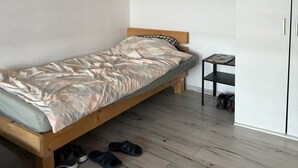 Yksi sänky kuviollisella peitolla, pieni pöytä lampun kanssa ja vaatekaappi minimalistisessa huoneessa.