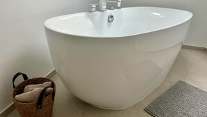 A modern bathroom with a freestanding bathtub, a small sink, and a wicker basket.