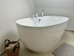 Ein modernes Badezimmer mit einer freistehenden Badewanne, einem kleinen Waschbecken und einem Korbwannen-Korb.