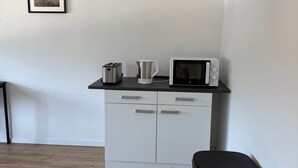 A kitchen with a microwave, toaster, and kettle on the countertop, a trash bin, and a framed picture on the wall.