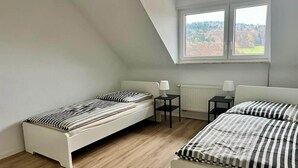 A bedroom with two single beds, a window with a view, a radiator, and a small table.