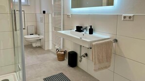 Moderni kylpyhuone, jossa on lasinen suihkuseinä, wc, peilillä varustettu pesuallas ja pyyhe, joka on ripustettu seinälle.