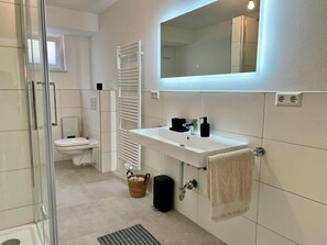 Un bany modern amb una cabina de dutxa de vidre, un vàter, un lavabo amb un mirall a sobre i una tovallola penjada a la paret.