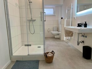 A modern bathroom with a glass shower enclosure, a toilet, a sink with a mirror, and a small window.