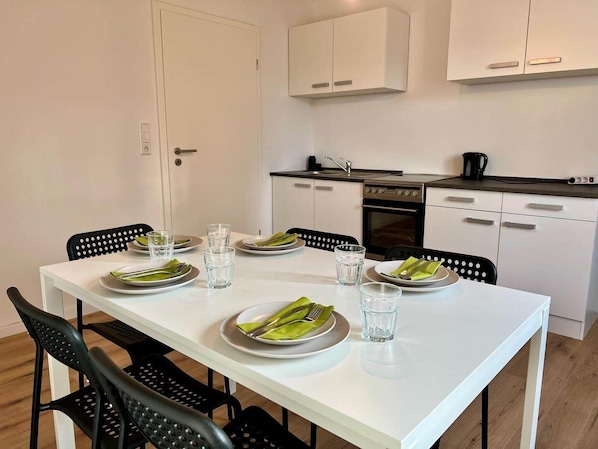 A modern kitchen with white cabinets, a dining table set with plates and glasses, and black chairs.