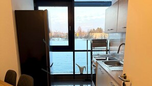 Eine kompakte Küche mit Blick auf ein Gewässer, ein Essbereich mit Tisch und Stühlen sowie eine Glastür zum Balkon.