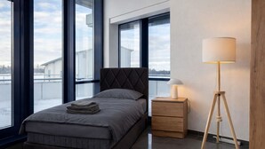 Ein modernes Schlafzimmer mit Bett, Nachttisch, Lampe und großen Fenstern.