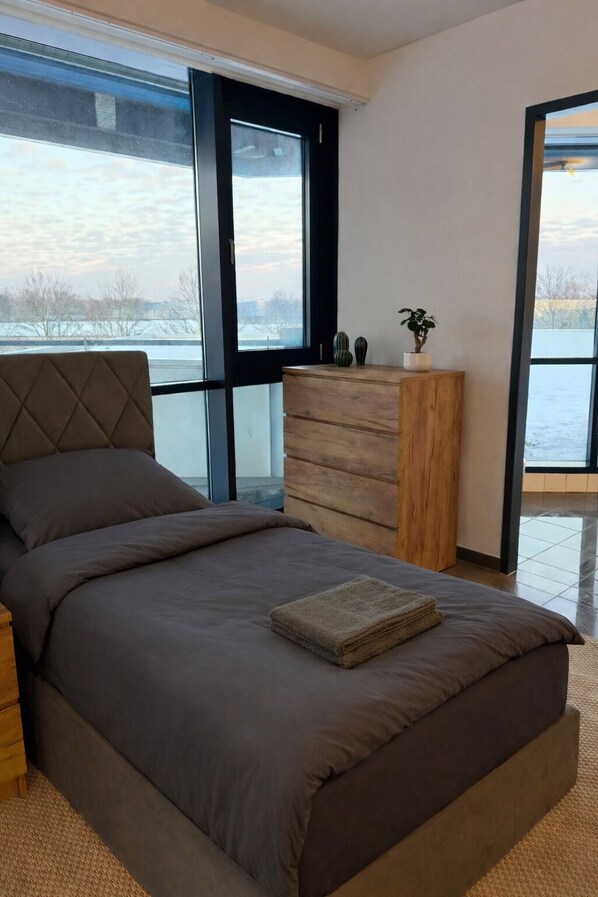 A modern bedroom with a large bed, a wooden dresser, and a view of a snowy landscape through a large window.