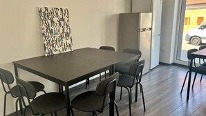 Moderni ruokailutila, jossa on pitkä pöytä, kuusi tuolia, jääkaappi ja suuri ikkuna, josta on näkymä kadulle.