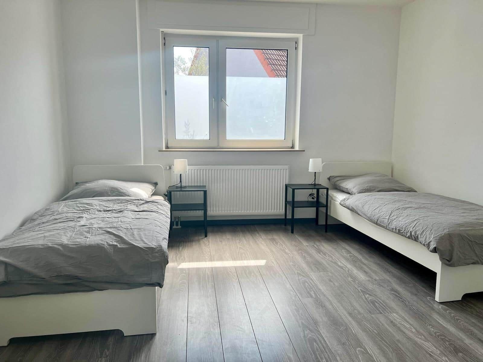 A small, clean room with two single beds, a window, and a radiator.