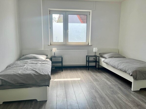 Ein kleines, sauberes Zimmer mit zwei Einzelbetten, einem Fenster und einer Heizung.
