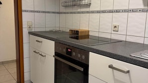 A kitchen with white cabinets, a black countertop, and a built-in oven. - Worker's apartment Rheinhausen (ground floor) (Oberhausen-Rheinhausen)