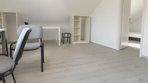 A room with a sloped ceiling, a dining table, chairs, a small stool, and built-in shelving. - Fitters' apartment Oberhausen-Rheinhausen, Lönsweg 3, DG (Oberhausen-Rheinhausen)