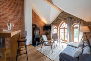 A loft-style room with a brick wall, a fireplace, a TV, a sofa, and a dining area with a table and chairs. - Elegant Retreat: Private Sauna, Whirlpool Bath and Fireplace - Last Minute (Grossharthau)